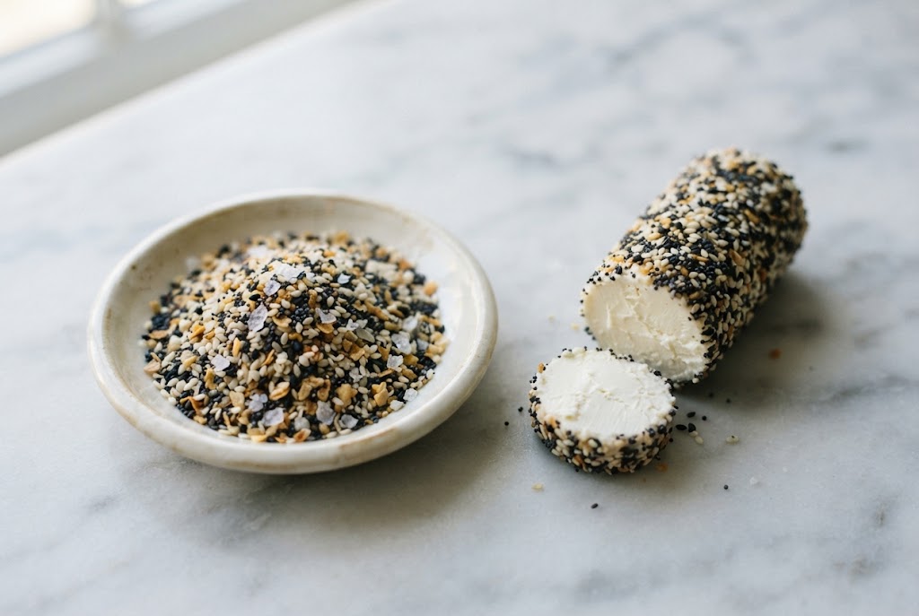 Everything Bagel Seasoning: speckled black and white seed mix, cream cheese log coated in it, on pale marble