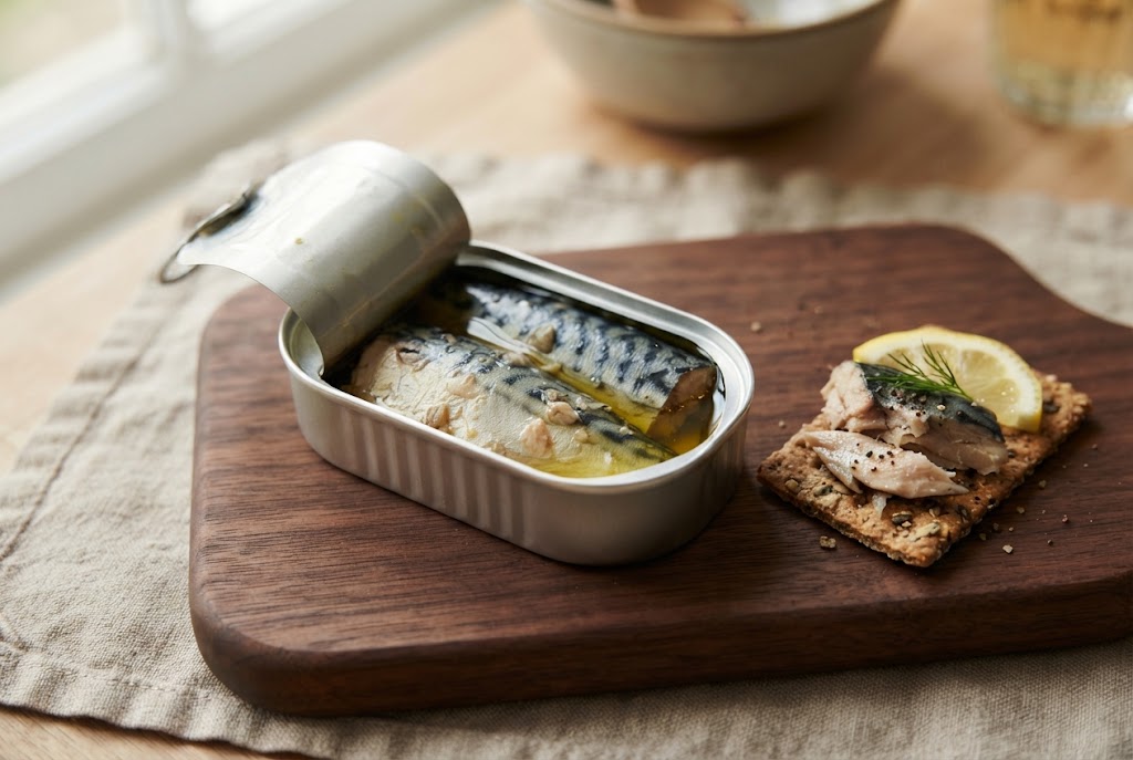 Tinned Mackerel: thick pale fillets with blue-striped skin in oil, on a dark walnut board
