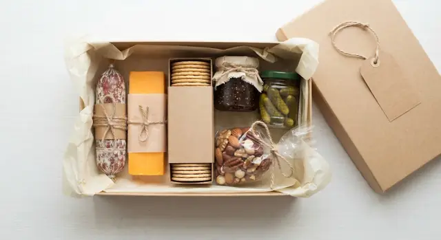 A small kraft gift box with a whole salami, cheddar, crackers, fig jam, cornichons and nuts